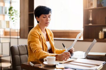 Middle Aged Business Woman Taking Notes Near Laptop In Office