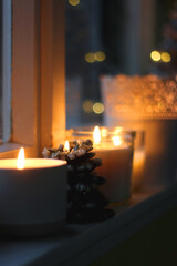 Lit candles and Christmas decorations on the window sill at night. Hygge at home. Selective focus.