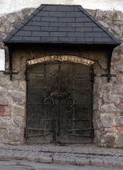 Fototapeta na wymiar Black metal door is under a canopy in old stone wall