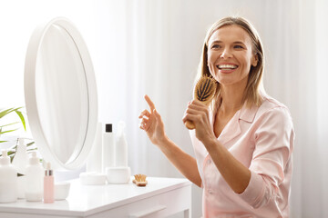 Haircare Concept. Cheerful Mature Female Having Fun While Brushing Hair At Home
