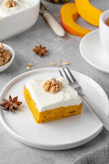 Spiced pumpkin cake with walnut and cream cheese frosting sliced into squares on a gray concrete background. Autumn dessert.
