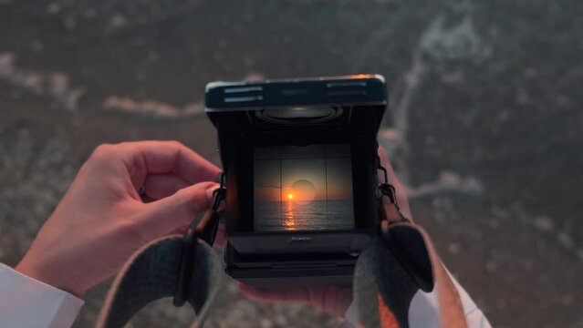 View through old film camera viewfinder. Female hands holding retro analogue tlr medium format 120 mm camera and taking picture of the sea on the beach at sunrise