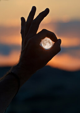 Silhouette of a man's hand making an ok sign in front of a full moon at sunset, Gozo, Malta