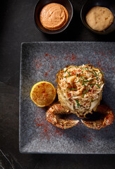 Top view close-up of cleaned crab meat with lemon, presented in a hairy crab with sauces on a gray stone plate, black background