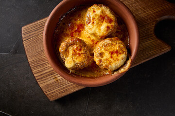 Close-up horizontal top view of baked mushrooms generously filled with suluguni cheese, presented on a Georgian 'keci' clay plate, beautifully contrasted on a wooden board with a dark background