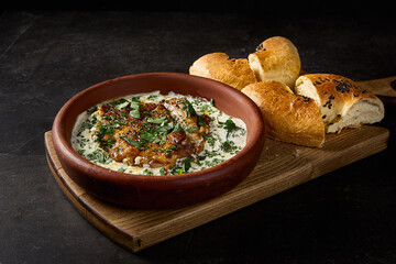 Side view in a horizontal frame of satsivi, a Georgian signature dish of chicken in walnut sauce, complemented by tandoor bread, set on a black canvas