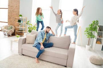 Full body portrait of four persons displeased tired man sit on sofa hand on head girls standing have fun indoors
