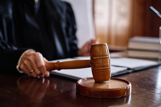 Judge of supreme court hitting sounding block with wooden gavel while sitting by desk in courtroom and passing judgement during trial session