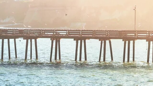 Colorful residential neighborhood Capitola Venetian Court in the California coast, USA. Aerial view of the old abandoned pier with many sea gulls and pelicans. Classical wooden pier.