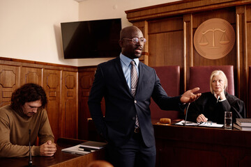 Confident attorney in formalwear speaking to prosecution side during trial session while standing...