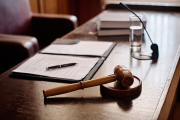 Wooden gavel on sounding block fixed on desk of judge with juridical documents in open folder with pen, microphone and glass of water