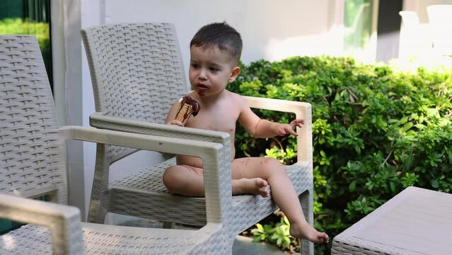 kid boy and baby eating ice cream in cone sitting on chair outdoor balcony garden terrace on park bench. cute siblings enjoying food outside. ice cream is melting, summer, vacation in hotel.