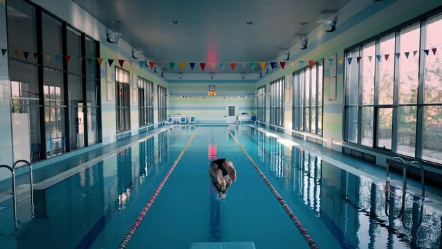 Slim athlete dives from podium to swim underwater in pool