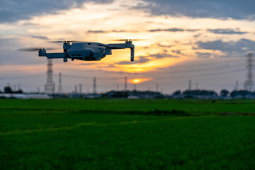 夕暮れの中、田んぼをホバリングするドローン