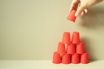 Pyramid of red plastic cups on desk. khaki beige background. teamwork balance business develop...