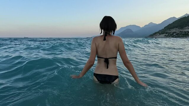 summer mood, relaxation by the sea on Turkish Riviera. Slow Mo Young asian woman in black swimsuit going for a swim in clean Mediterranean Sea