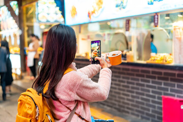 Young female tourist taking a photo of street food at  Jinli Ancient Street in Chengdu, China