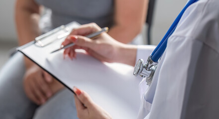 Fototapeta premium The female doctor gives advice to patient and recommends ways to take care of their health and writes down medical prescription.
