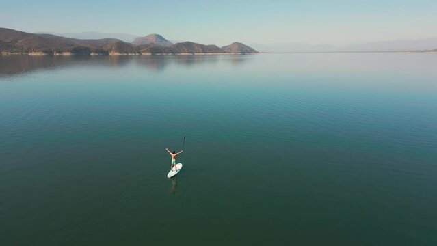 Aerial drone flying over a lake, man doing stand up paddle, with mountains at sunrise. SUP. Beautifull dreamy landscape view. Cosatline with boats. Paceful landscape. Cabra Corral, Salta, Argentina.