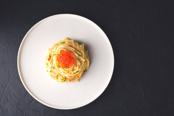 Spaghetti pasta with red caviar on a black background.   Delicatessen seafood pasta. Dark key mood, minimalism, magical light in the style of the Chef's table. Front view, copy space