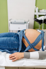Beautiful young pregnant woman at electrocardiograph check up for baby health and expected date of birth. Fetal heart monitoring. Healthcare and medical service concept.