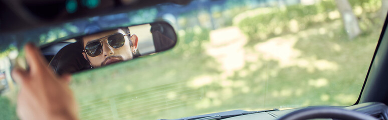good looking young sexy man with stylish sunglasses looking at his rearview mirror, banner