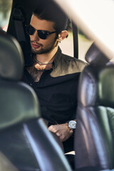 handsome male model with dapper look in sunglasses sitting on backseat of his car, fashion and style