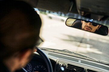 handsome sexy male model with sunglasses behind steering wheel and looking in rearview mirror - obrazy, fototapety, plakaty