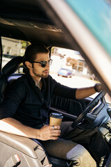 Fototapeta na wymiar tempting driver with earring and wristwatch holding coffee cup while sitting behind steering wheel