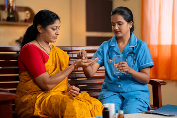 Caretaker or Nurse giving medicines to patient at home - concept of home health care service,...