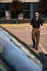 good looking young male model in black vivid attire walking to his car with hand in pocket, fashion