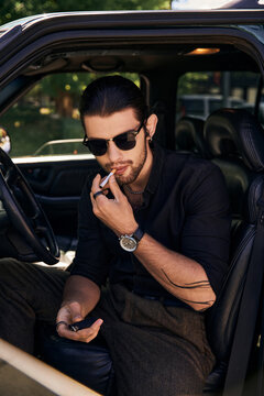 appealing young male model with wristwatch and tattoo in elegant black attire posing with cigarette