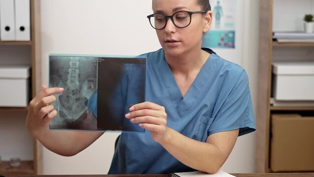 Woman traumatologist points finger at X-ray picture talking to patient online looking at camera doctor consults visitor remotely treatment in modern clinic