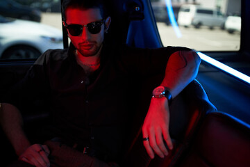 good looking man in stylish black shirt with sunglasses looking at camera sitting in his car