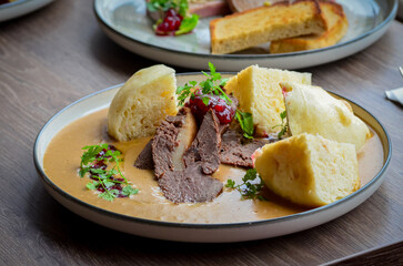 traditional Czech food served on a wooden table, cream sauce, dumpling, beef, cranberries, wild dear or beef meat