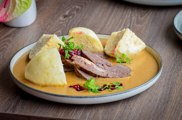 traditional Czech food served on a wooden table, cream sauce, dumpling, beef, cranberries, wild dear or beef meat