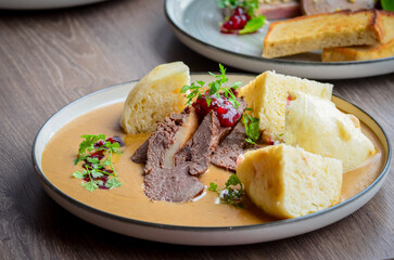 traditional Czech food served on a wooden table, cream sauce, dumpling, beef, cranberries, wild...