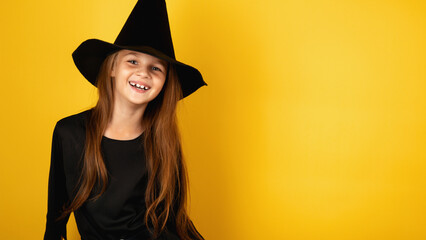 little girl in a Halloween witch costume on a yellow background. Halloween for children, space for text