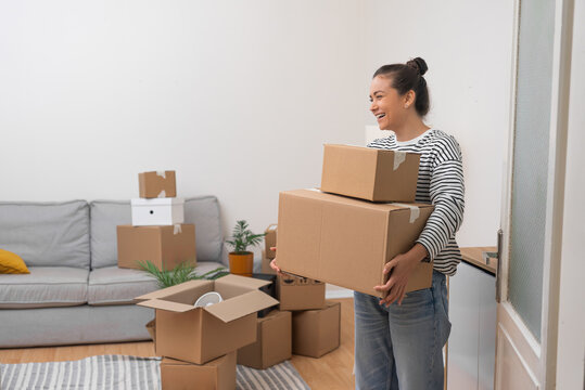 Cheerful woman holds packed boxes with household goods moving to new apartment in light shades positive emotions from changing place of residence in modern city