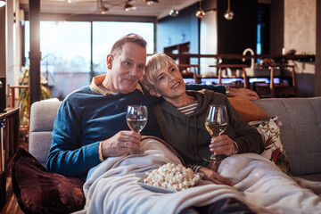 Affectionate senior couple enjoying wine and popcorn during a cozy evening at home