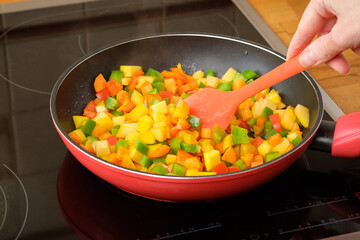 Stirring fry chopped vegetables - red pepper, carrot and pumpkin in a pan. Cooking healthy gluten free vegan and vegetarian food.