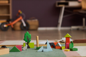 Close up of wooden toys and bricks on colorful carpet in playroom, copy space
