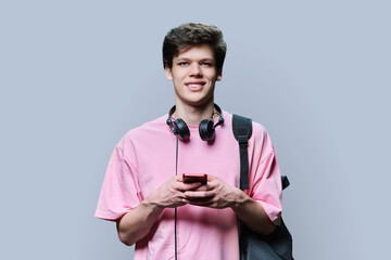 Young male with headphones holding smartphone, on grey background