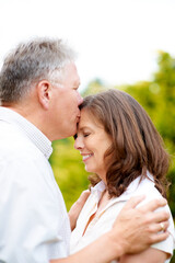 Fototapeta premium Senior man, kissing and wife on forehead in park, care and people love for commitment in marriage. France, couple and wellness in nature to connect, hug and happy together in support family on date