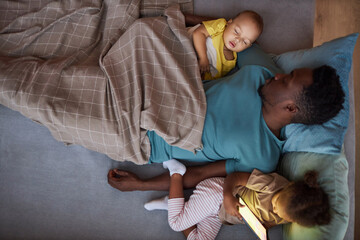 Top down view of exhausted African American man sleeping with two little children at nap time