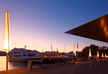 Naklejka premium Morning scenery of beautiful Lake Lucerne at sunrise with view of cruise ships parking at the dock by Culture & Congress Center and golden light of dawning sky reflected on peaceful water in twilight