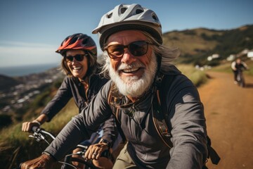 Fototapeta premium Elderly smiling couple in safety helmets ride bicycles together to stay fit and healthy. Happy African American seniors having fun on a bike ride on country road. Retired people lead active lifestyle.