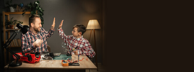 Teen boy giving high five to his father after fixing of electronic toy car. Concept of educational process. Copy space