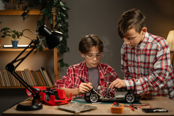 Brothers soldering wires for machine at home in the evening. Children studying technology and electronics in the workshop.