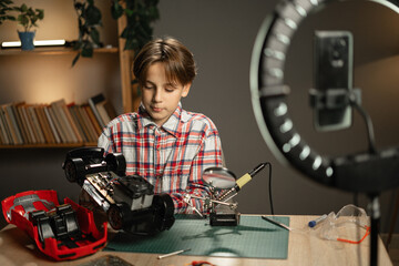 young blogger boy records social media videos at home, showcasing his toy repair skills with a robot and soldering iron, creating a glimpse into the future of mechanized play.